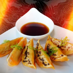 A plate of Gyoza with a bowl of sauce.